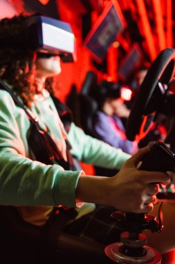 VR kulaklıklı bulanık Afrikalı Amerikalı kız araba yarışı simülatöründe oyun oynuyor