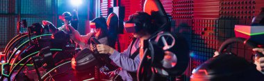 VR kulaklıklı genç arkadaşlar araba yarışı simülatörlerinde oyun oynuyorlar.
