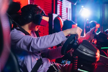 Araba simülatöründe yarış oyunu oynayan VR kulaklıklı genç çocuk.