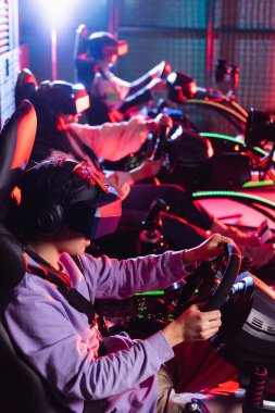 VR kulaklıklı gençler bulanık arka planda araba simülatörlerinde yarışıyorlar.