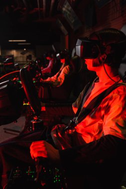 teenager in vr headset racing on car simulator near blurred friends clipart