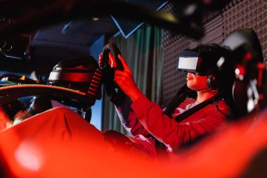 VR kulaklıklı genç araba yarışı simülatöründe bulanık ön planda oyun oynuyor