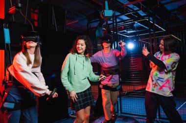 teenage boy taking photo of cheerful interracial friends in vr game zone clipart