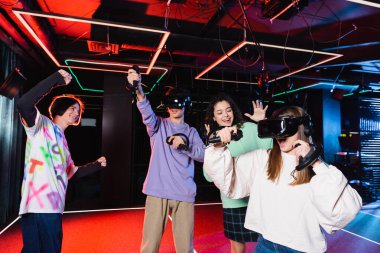 VR oyun odasındaki çok kültürlü arkadaşlarının yanında kazanan jest gösteren neşeli genç çocuk.