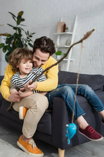 Feliz Padre Hijo Jugando Juguete Pesca Sofá —  Fotos de Stock