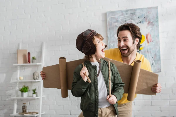 Chico Excitado Alas Cartón Casco Aviador Pie Cerca Papá Casa — Foto de Stock