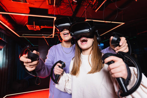 thrilled teenage gamers in vr headsets having fun in play zone