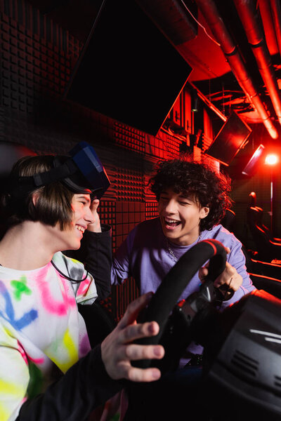 веселые подростки разговаривают рядом с автомобильным тренажером в игровой комнате