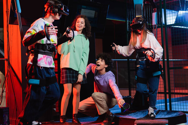 excited multicultural teenagers looking at friends gaming on vr platform