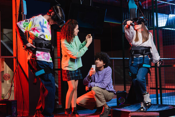 interracial teenagers taking photo of friends gaming in vr headsets