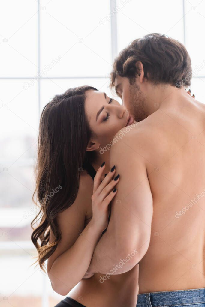 Muscular man kissing pretty woman at home 