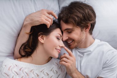 Gülümseyen adamın yatakta kız arkadaşının burnuna dokunuşunun en üst görüntüsü. 