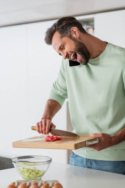 Heyecanlı adam taze salata hazırlarken gülüyor ve akıllı telefondan konuşuyor.