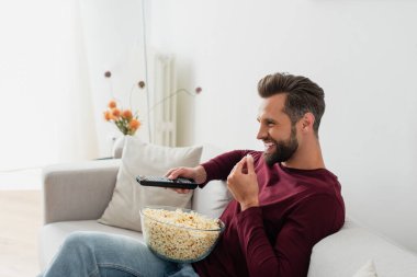 laughing man eating popcorn while watching comedy film in living room clipart