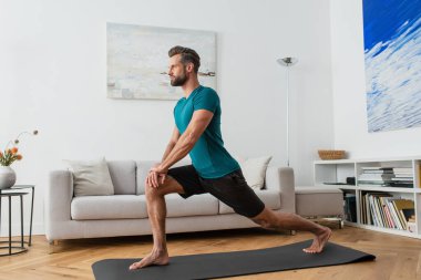 sportif adam evdeki yoga minderinde hilal hareketi yapıyor.