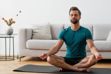 Kapalı gözlü bir adam nilüfer çiçeğiyle meditasyon yapıyor yoga minderinde poz veriyor.