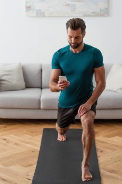 Çıplak ayaklı adam evde yoga yaparken akıllı telefona bakıyor.