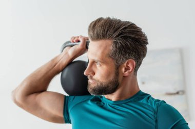 Atletik adam evde kettlebell egzersizi yaparken gözlerini kaçırıyor.