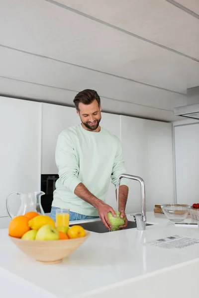 Hombre Sonriente Lavando Lechuga Mientras Prepara Desayuno Cerca Frutas Frescas —  Fotos de Stock