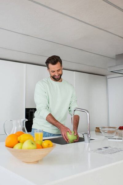 smiling man washing lettuce while preparing breakfast near fresh fruits