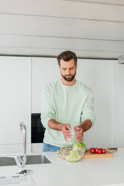 man preparing salad from fresh vegetables for breakfast