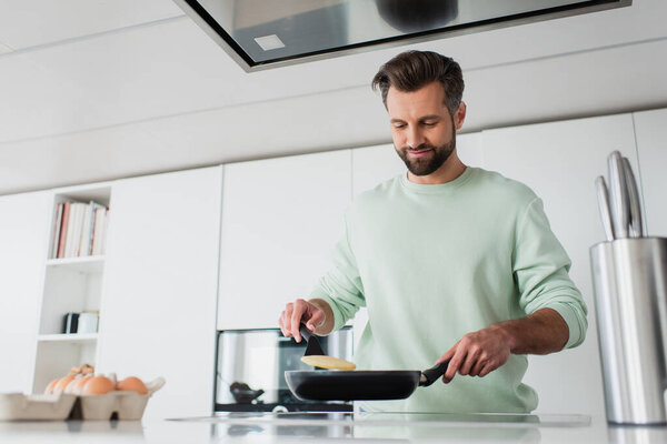 Радостный мужчина готовит блины на завтрак на кухне