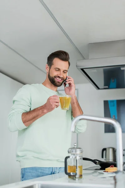キッチンで携帯電話で緑茶を飲んで陽気な男 — ストック写真