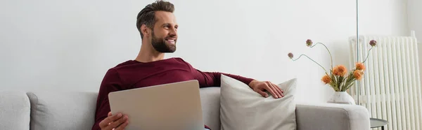 Sorrindo Homem Olhando Para Longe Enquanto Sentado Sofá Com Laptop — Fotografia de Stock