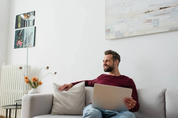 Homem Positivo Sorrindo Enquanto Sentado Sofá Casa Com Laptop — Fotografia de Stock