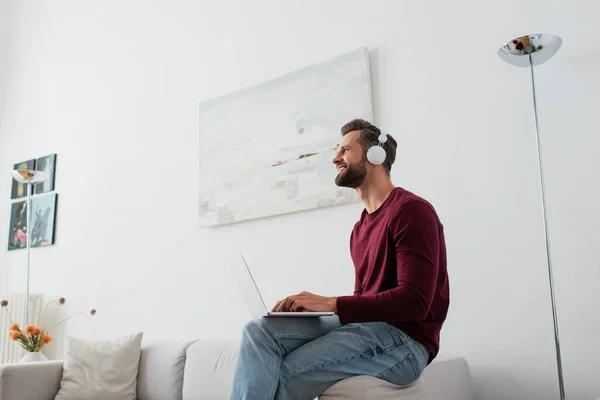 Gelukkig Man Hoofdtelefoon Weg Kijken Terwijl Zitten Bank Met Laptop — Stockfoto