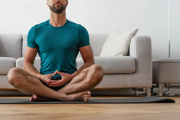 cropped view of barefoot man meditating in lotus pose at home