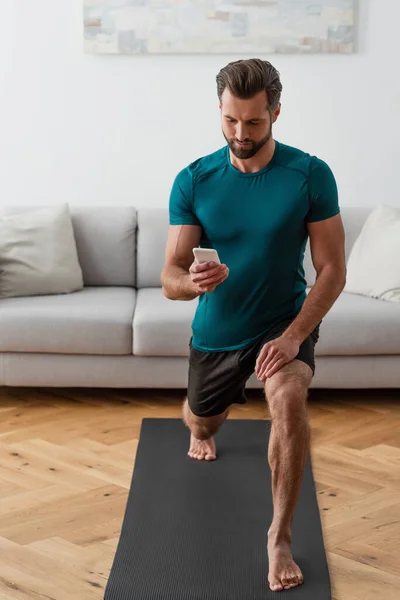 barefoot man looking at smartphone while practicing yoga at home