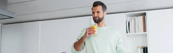 Vreugdevolle Man Die Wegkijkt Terwijl Hij Een Glas Sinaasappelsap Vasthoudt — Stockfoto