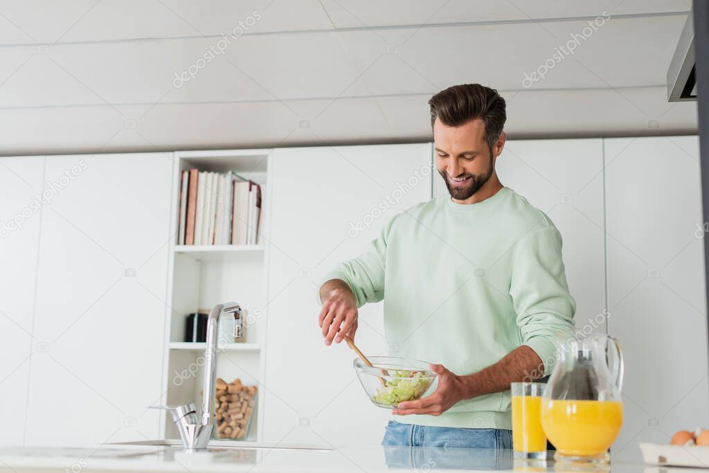 smiling man preparing fresh vegetable salad in kitchen