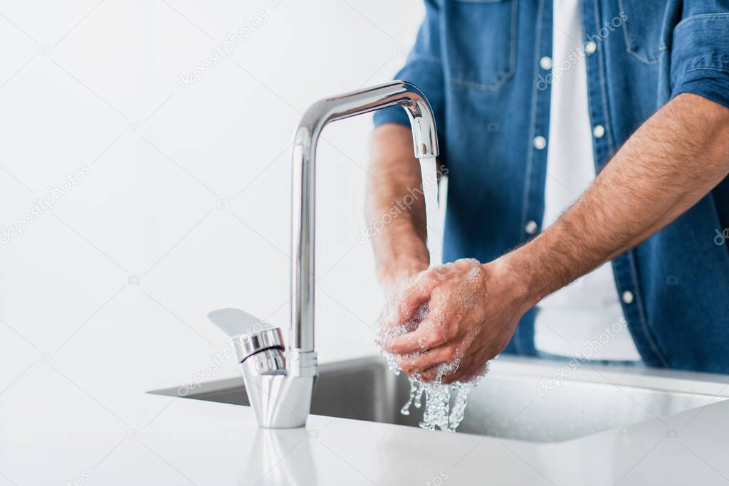 cropped view of man in denim shirt washing hands on blurred background