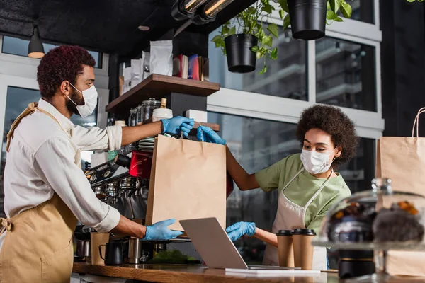 Camarero Afroamericano Máscara Médica Dando Bolsa Papel Colega Cerca Portátil — Foto de Stock