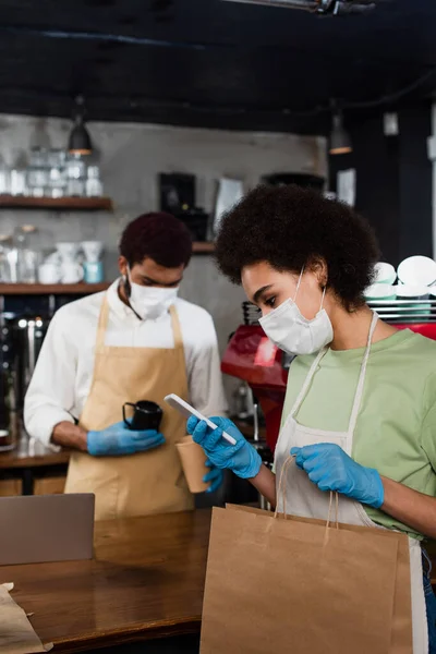 Africano Americano Barista Máscara Médica Usando Smartphone Segurando Saco Papel — Fotografia de Stock