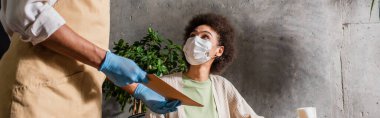 Plastik eldivenli Afro-Amerikan garson elinde tıbbi maskeli müşterinin yanında menü tutuyor. 