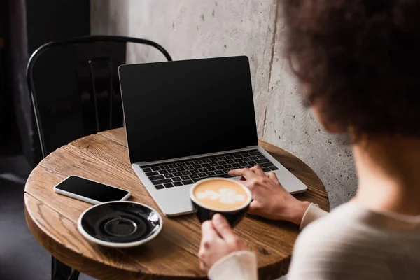 カフェでコーヒーとブラブリングフリーランサーの近くのノートパソコンやスマートフォン — ストック写真
