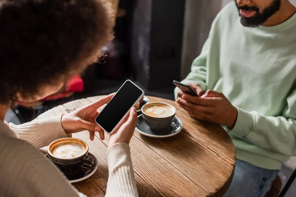 非洲裔美国妇女手握空白屏幕的智能手机 坐在男友旁边 咖啡在咖啡店里 — 图库照片
