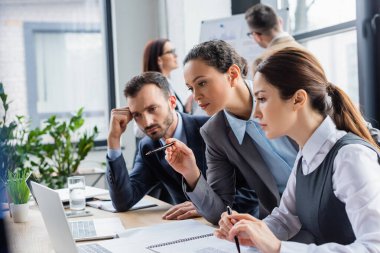 Ofisteki bulanık meslektaşlarının bilgisayarına işaret eden Afrikalı Amerikalı iş kadını. 