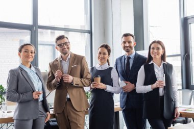 İçkili ve akıllı telefonlu ırklar arası iş adamları kameraya gülümsüyor. 