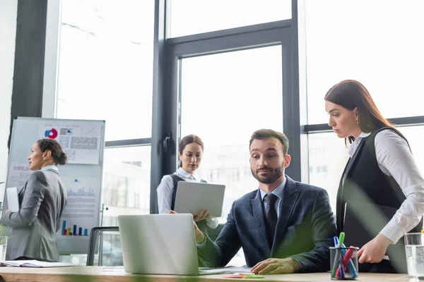 Affärskvinna Med Pappersmapp Tittar Kollega Nära Bärbar Dator Kontoret — Stockfoto