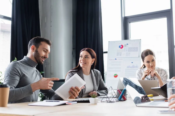 Affärsman Som Pekar Digital Surfplatta Nära Leende Kollega Vid Arbetsbordet — Stockfoto