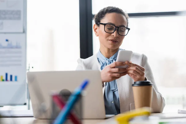 Afrykański Amerykański Bizneswoman Pomocą Smartfona Pobliżu Kawy Laptopa Biurze — Zdjęcie stockowe