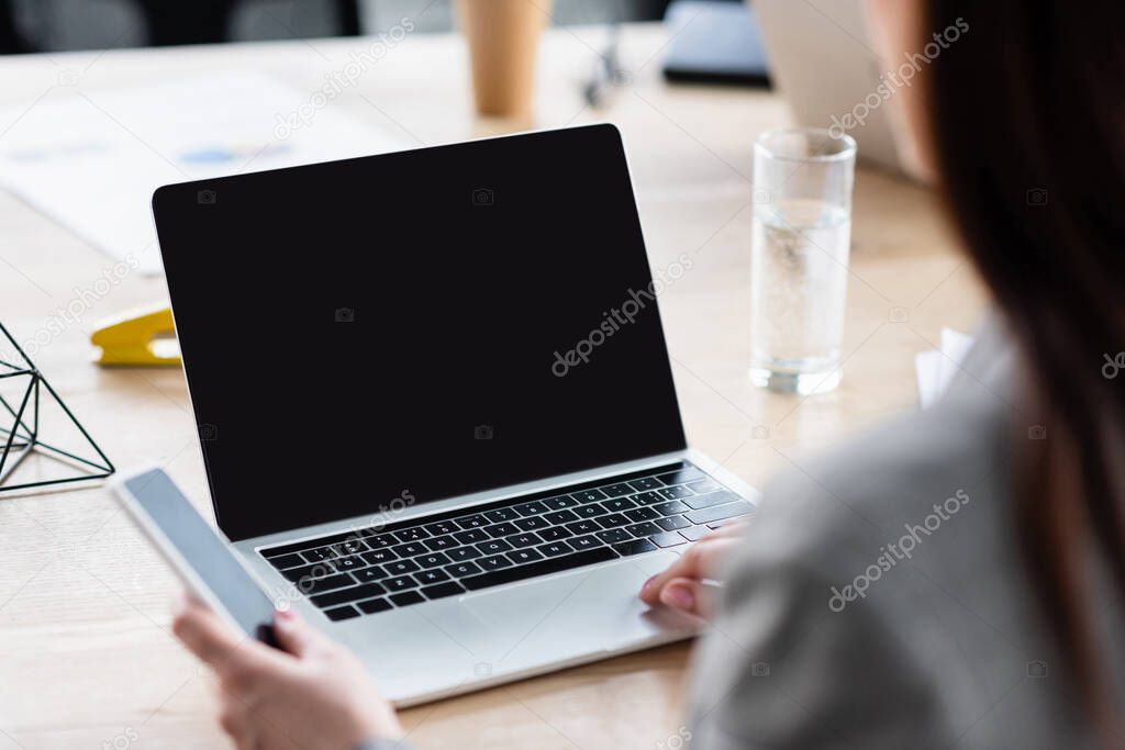 Cropped view of businesswoman using laptop and smartphone with blank screen 