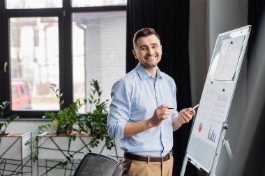 Kalem ve akıllı telefonlu mutlu yönetici resim çizelgesinin yanında duruyor 