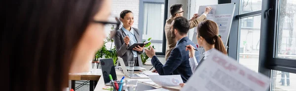 African american businesswoman with notebook near colleagues and flipchart in office, banner