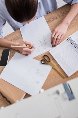 Overhead view of seamstress drawing sketch near notebook and smartphone  clipart