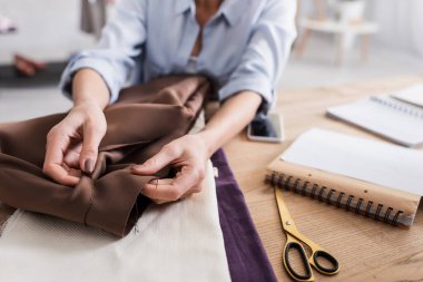 Makas ve defterin yanında kumaş tutan bulanık tasarımcının kırpılmış görünümü 